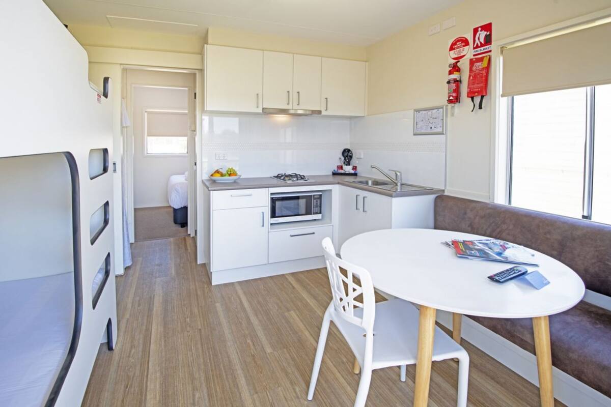 A compact kitchen with white cabinets, a microwave, and a sink. There's a dining area with a white table and chairs, and a sofa.