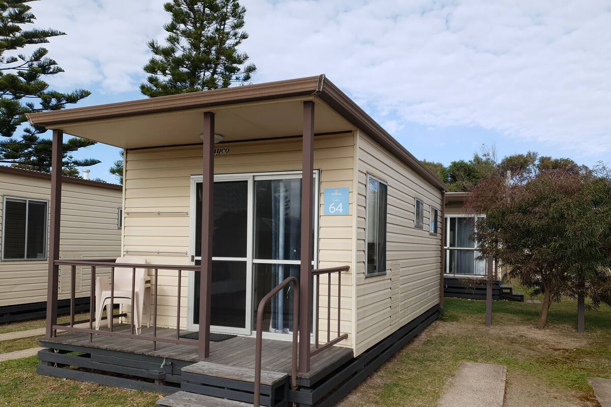 A single-story mobile home with a covered porch, a sliding door, and a small set of stairs leading to the entrance.