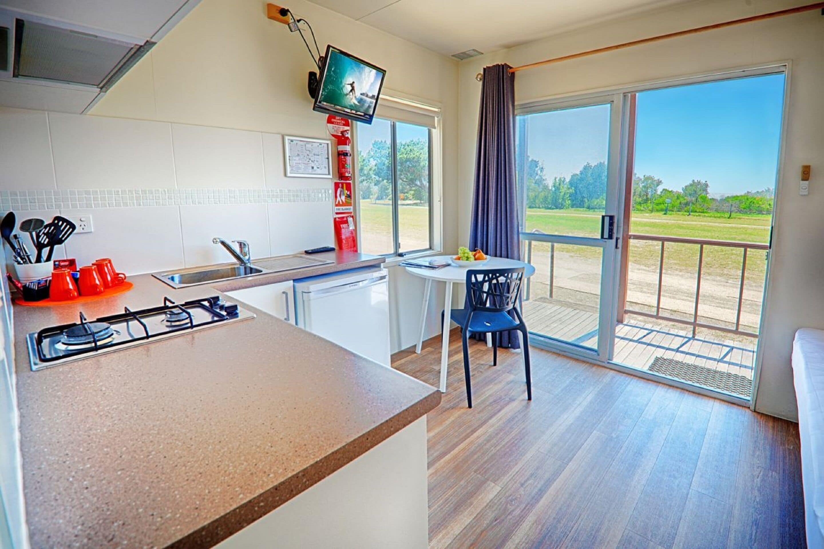 A modern kitchen with a gas stove, a dining area with a table and chairs, and a balcony with a view of the outdoors.