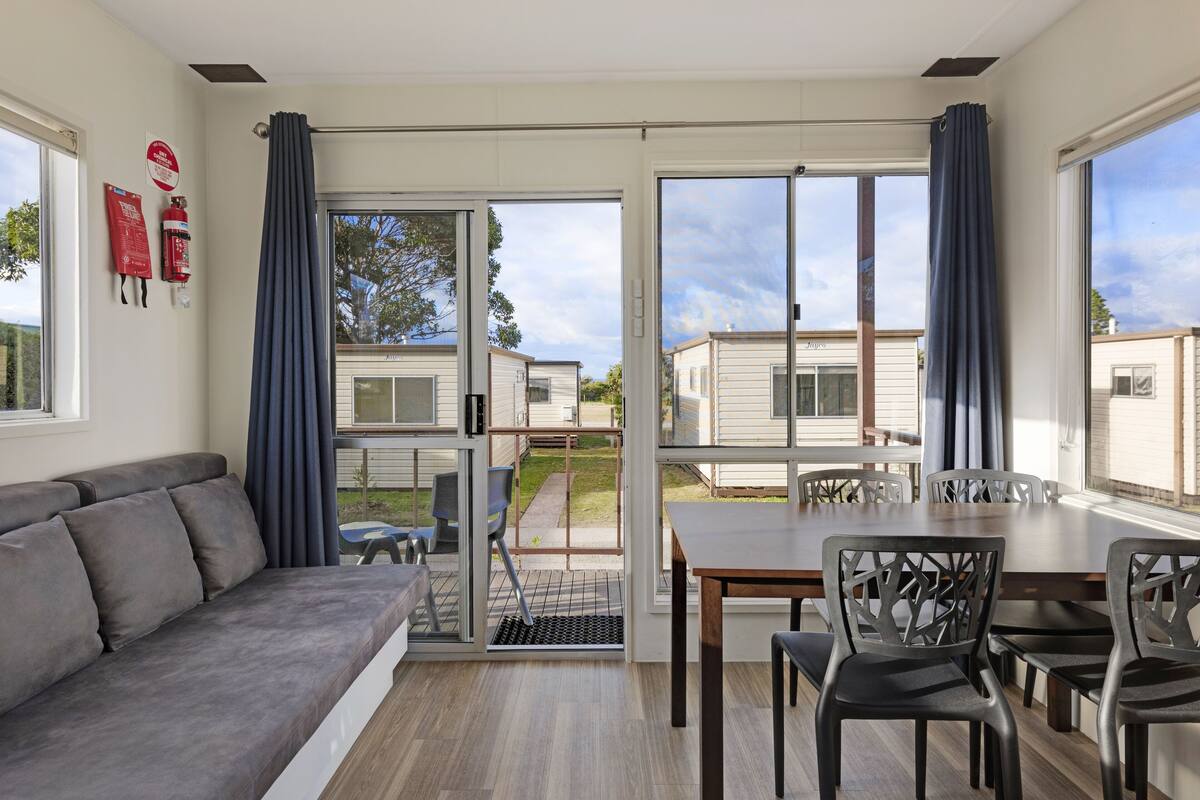 A modern living room with a grey sofa, a dining table with chairs, and large sliding glass doors leading to a patio.