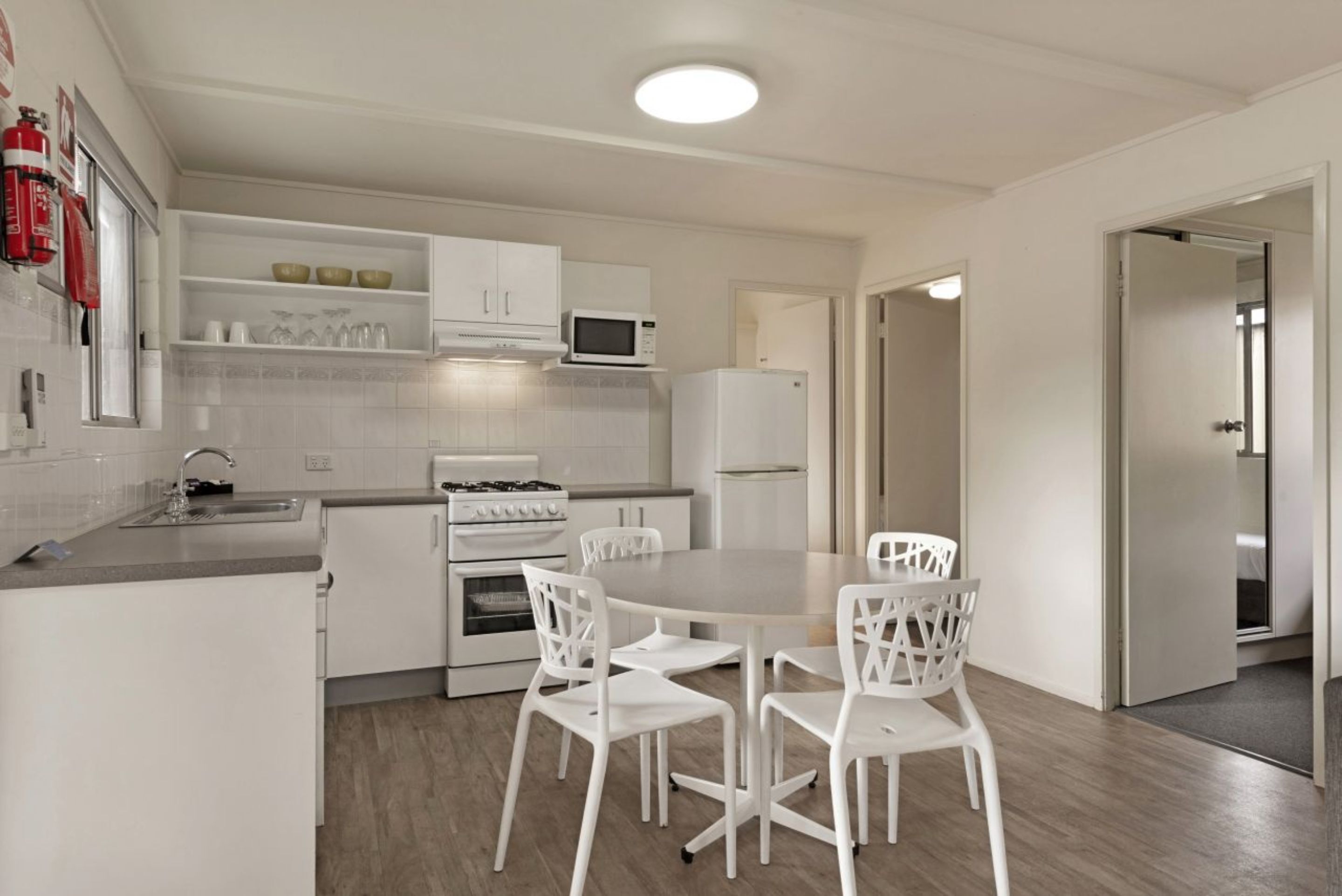 A modern kitchen with white cabinetry, a microwave, stove, and a dining area with white chairs.