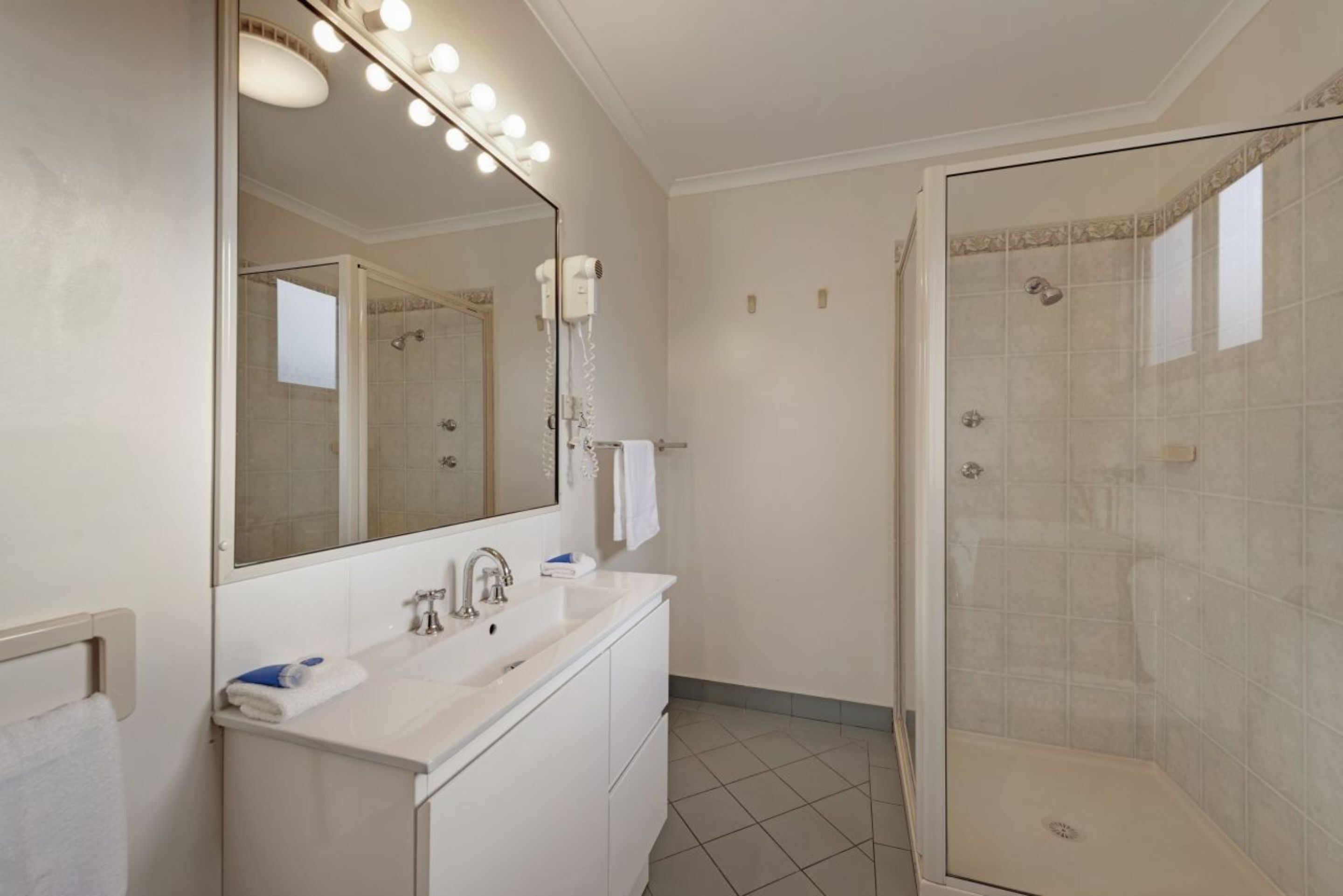 Un baño con un espejo grande, un lavamanos, una ducha y un tocador.