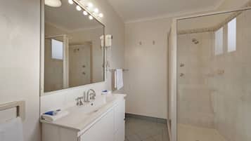 Un baño con un espejo grande, un lavamanos, una ducha y un tocador.