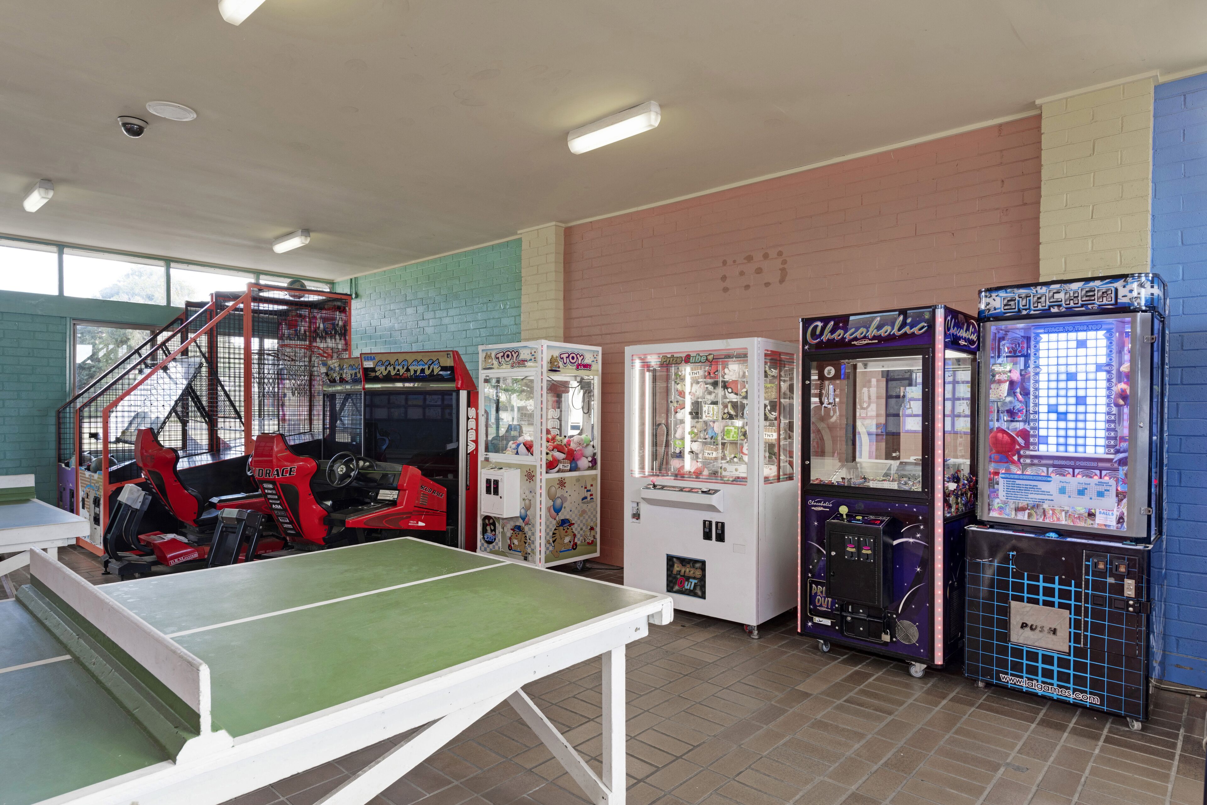 A gaming area with arcade machines, a ping pong table, and a staircase.