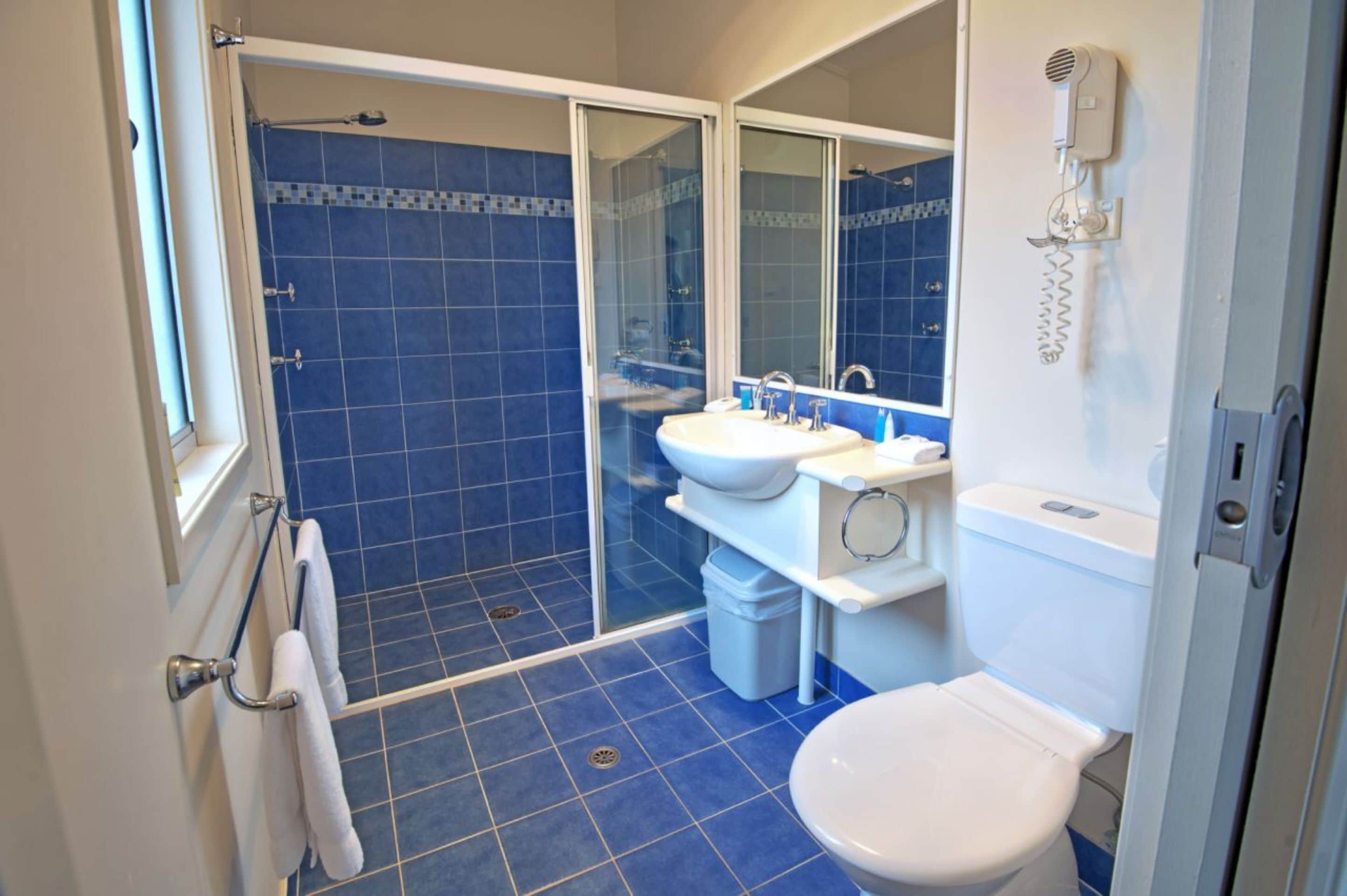 A bathroom with a shower, toilet, sink, and a mirror.