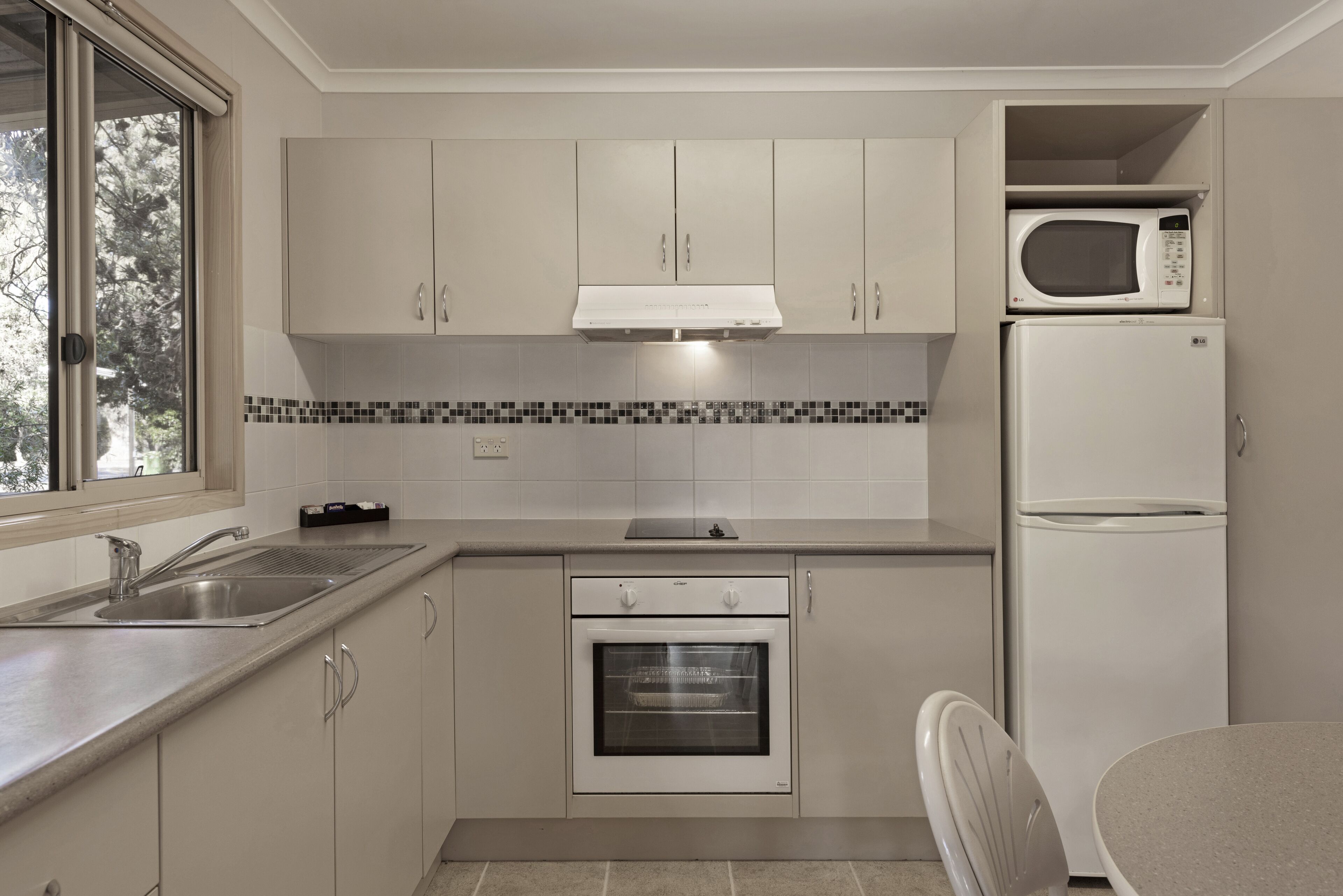 A modern kitchen with white cabinets, a built-in oven, a microwave, and a sink.
