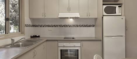 A modern kitchen with white cabinets, a built-in oven, a microwave, and a sink.