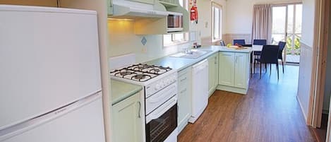 Une cuisine équipée d’une cuisinière, d’un four et de placards, qui donne sur un coin repas avec une table et des chaises.