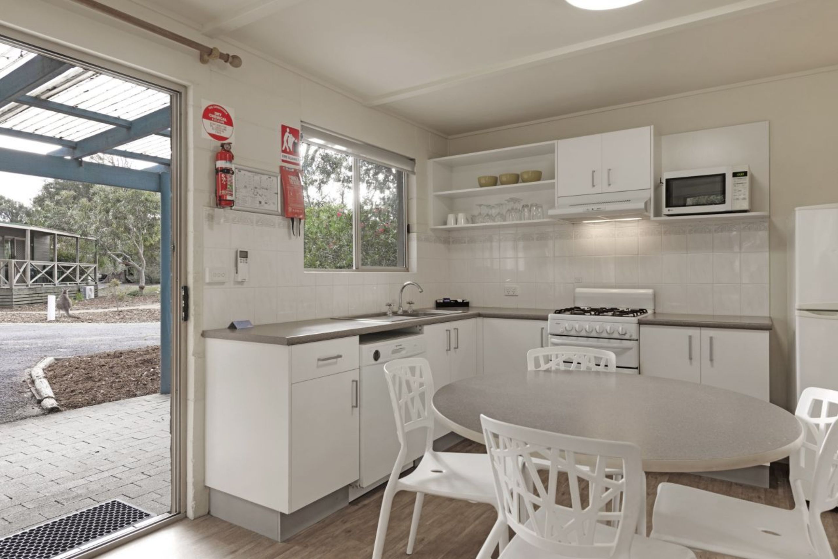 A modern kitchen with white cabinets, a gas stove, a microwave, and a dining area with white chairs.