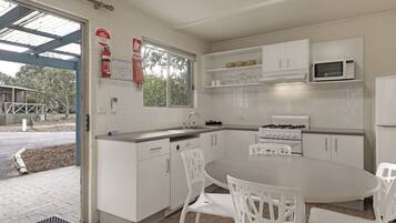 A modern kitchen with white cabinets, a gas stove, a microwave, and a dining area with white chairs.