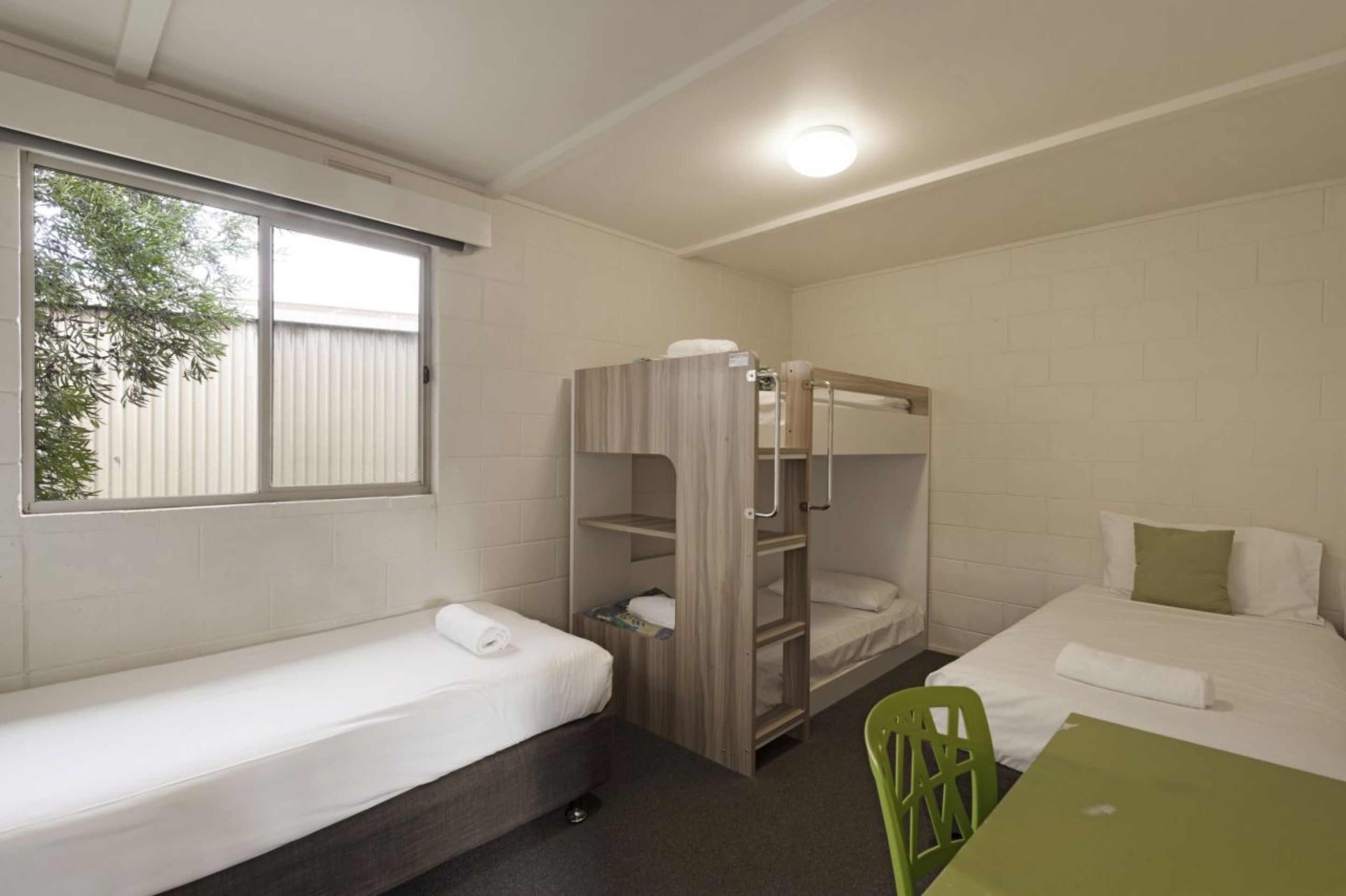 A dormitory room with bunk beds, a single bed, a green chair, and a table.