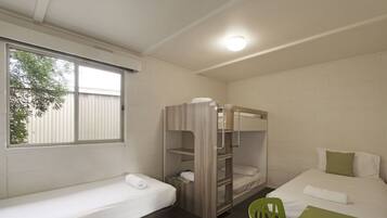 A dormitory room with bunk beds, a single bed, a green chair, and a table.