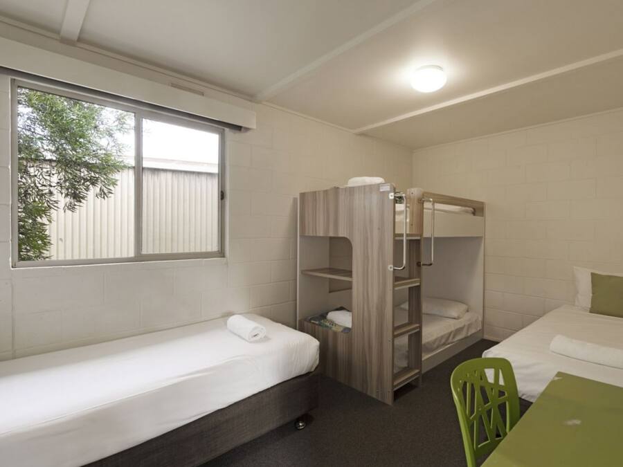 A dormitory room with bunk beds, a single bed, a green chair, and a table.