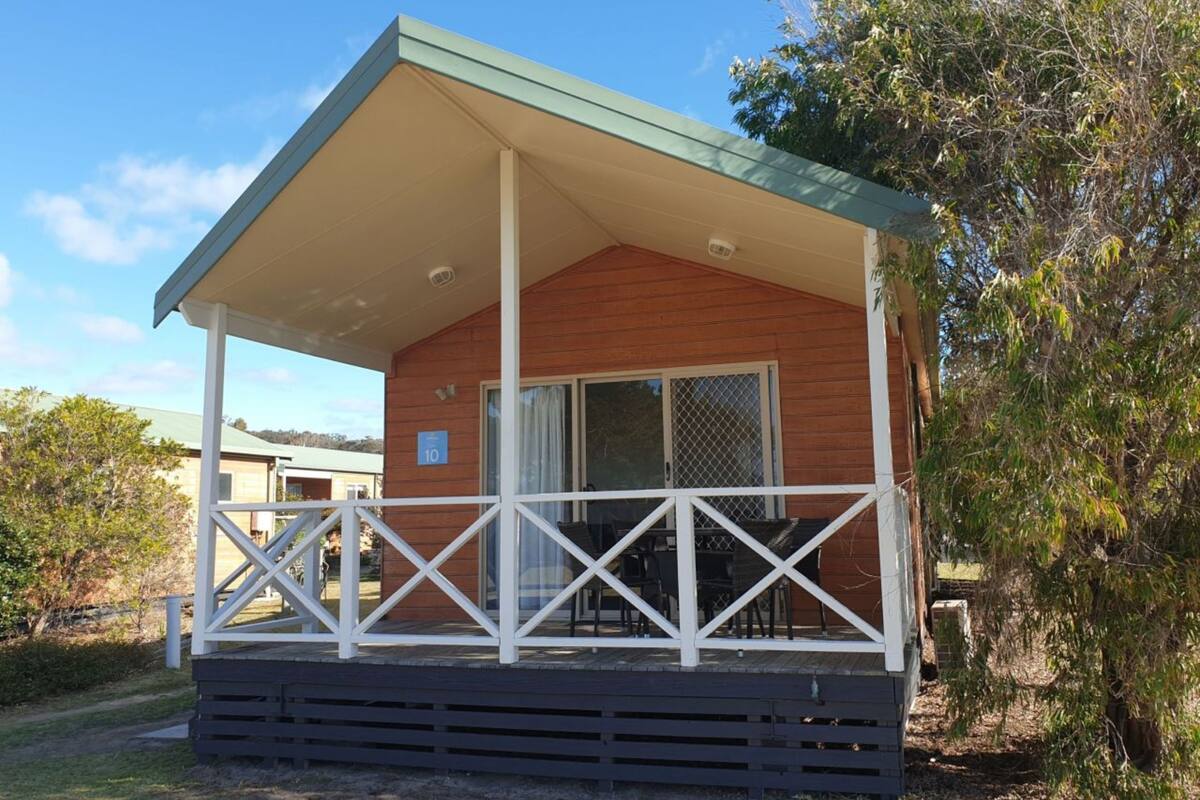 A single-story wooden cabin with a covered porch, a sliding glass door, and a small outdoor seating area.