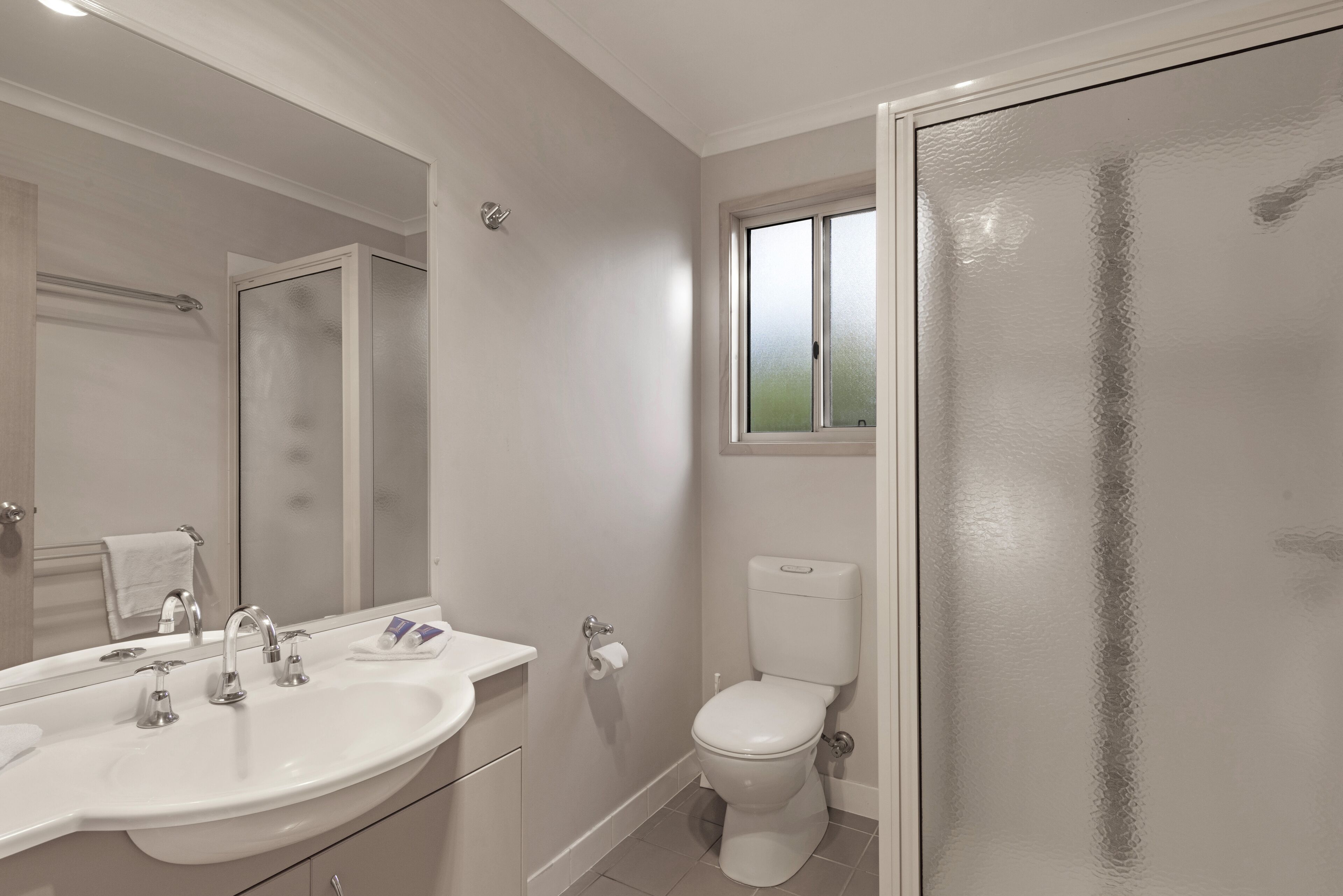 Un bagno con un lavandino bianco, due rubinetti, un water e una porta doccia in vetro satinato.