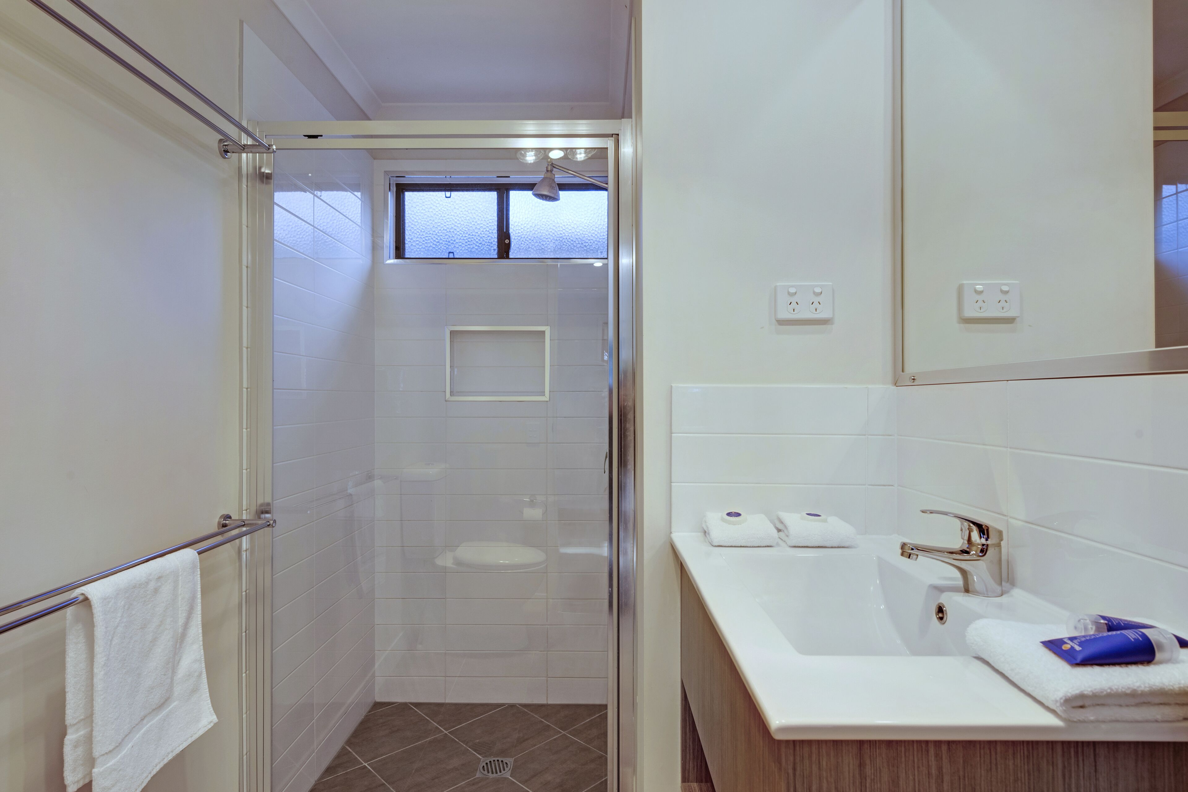 A modern bathroom with a glass shower enclosure, a white sink with a vanity, and a large mirror.