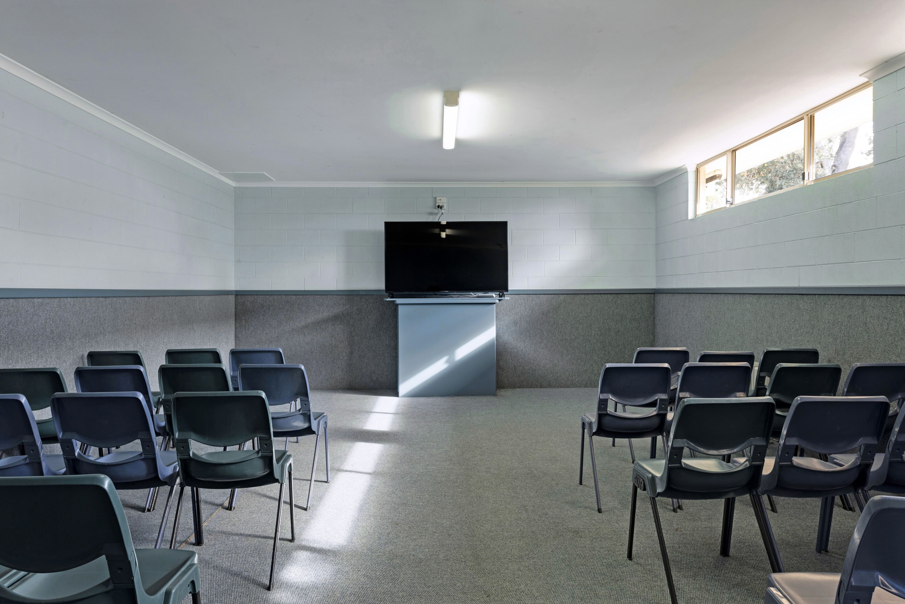 Une salle de conférence avec des rangées de chaises, un téléviseur à écran plat et un pupitre.