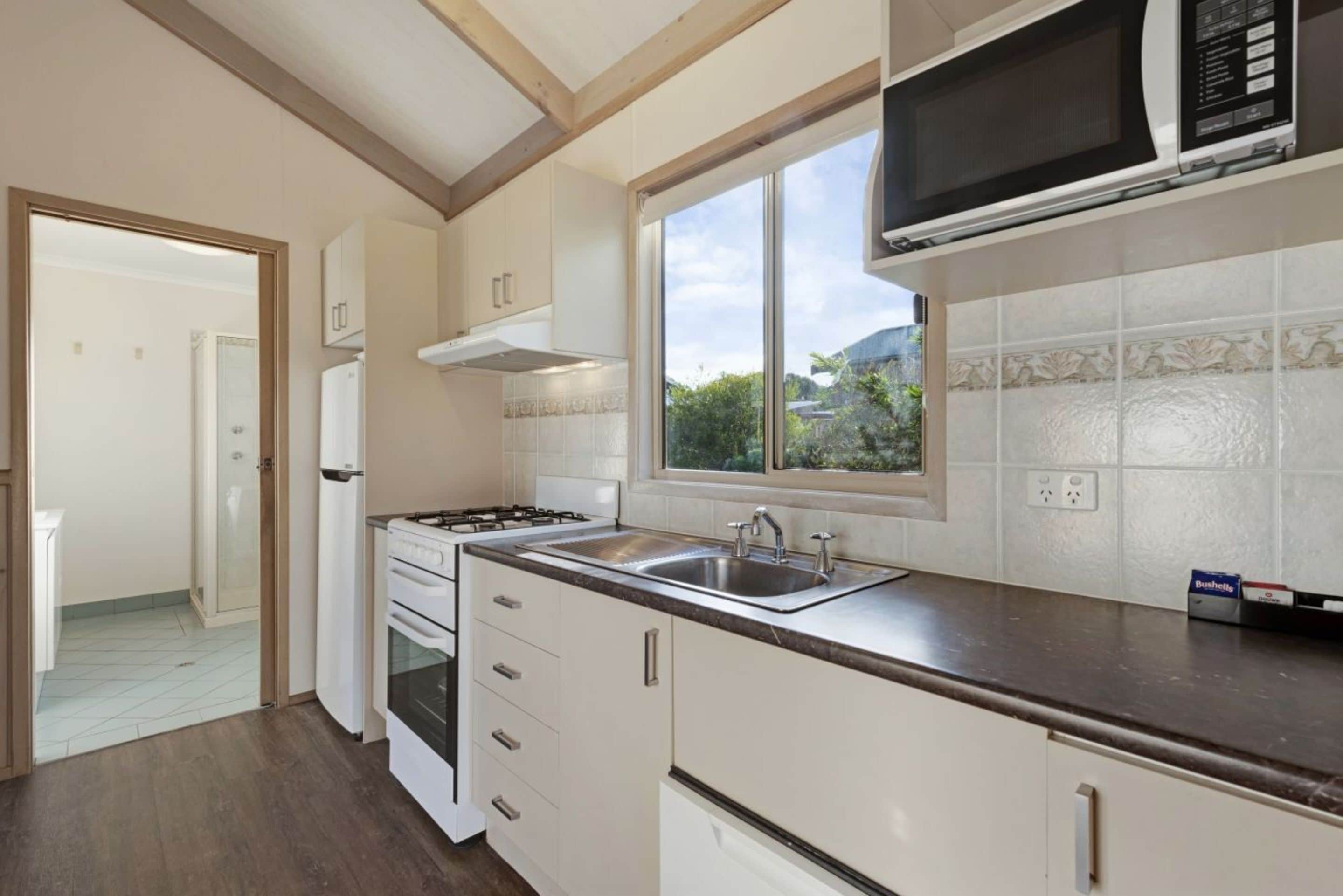 A kitchen with white cabinets, a stove, a sink, and a microwave.