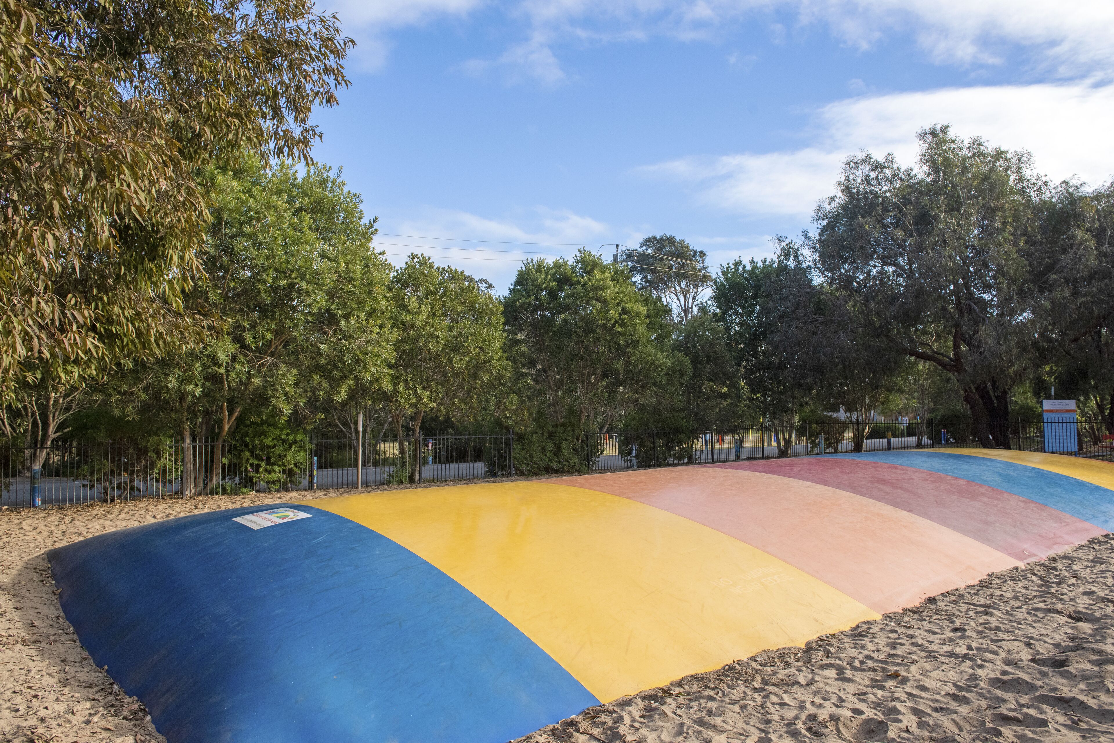 A colorful playground with a blue, yellow, and red slide, surrounded by trees and a fence.