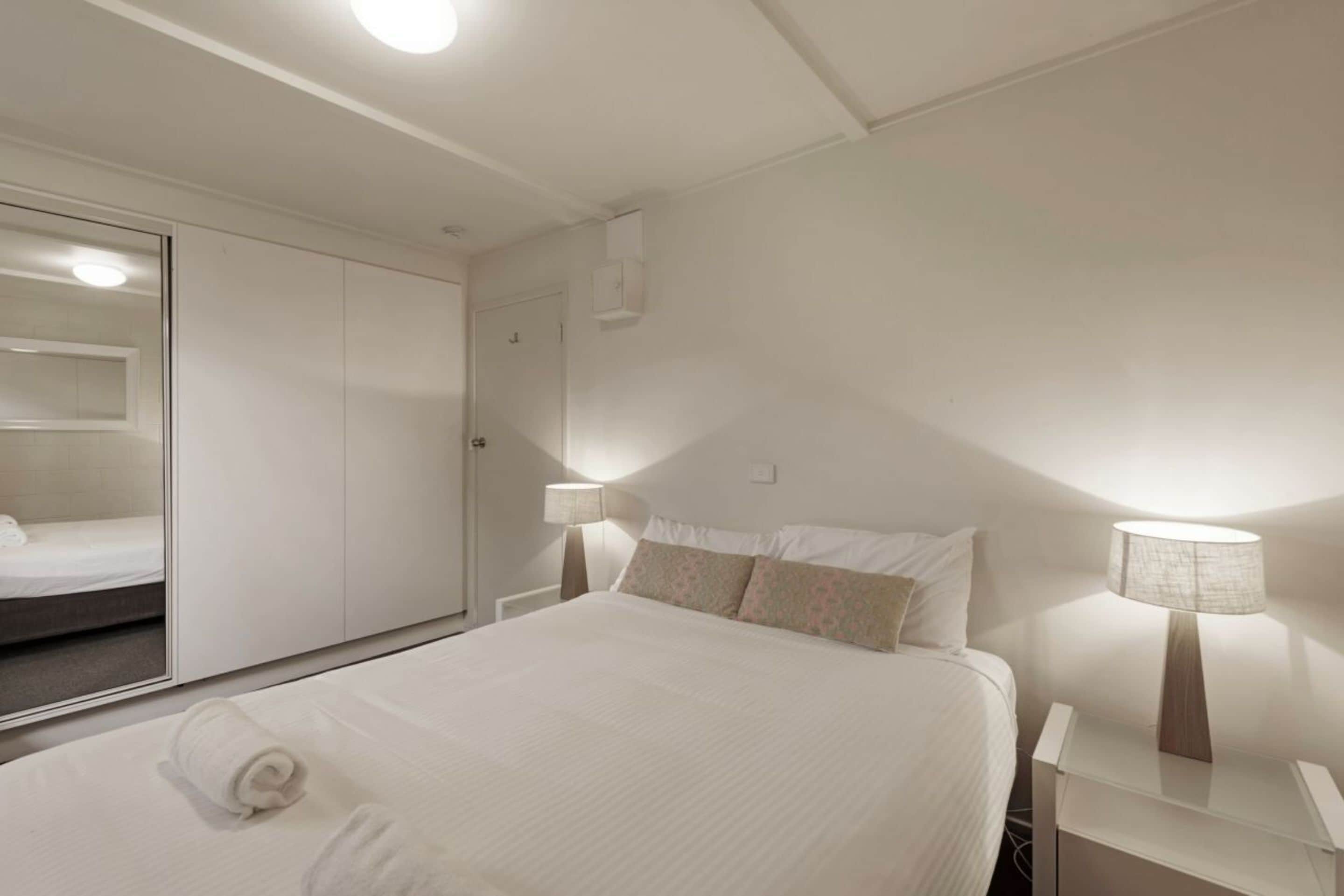 A hotel room with a bed, bedside lamps, a wardrobe, and a mirror.
