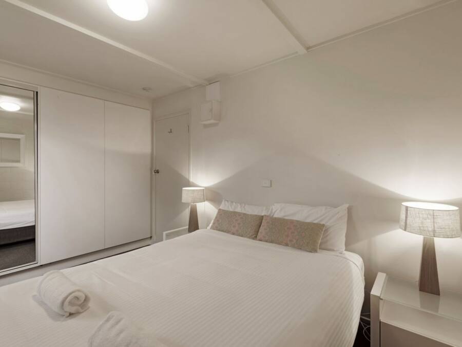 A hotel room with a bed, bedside lamps, a wardrobe, and a mirror.