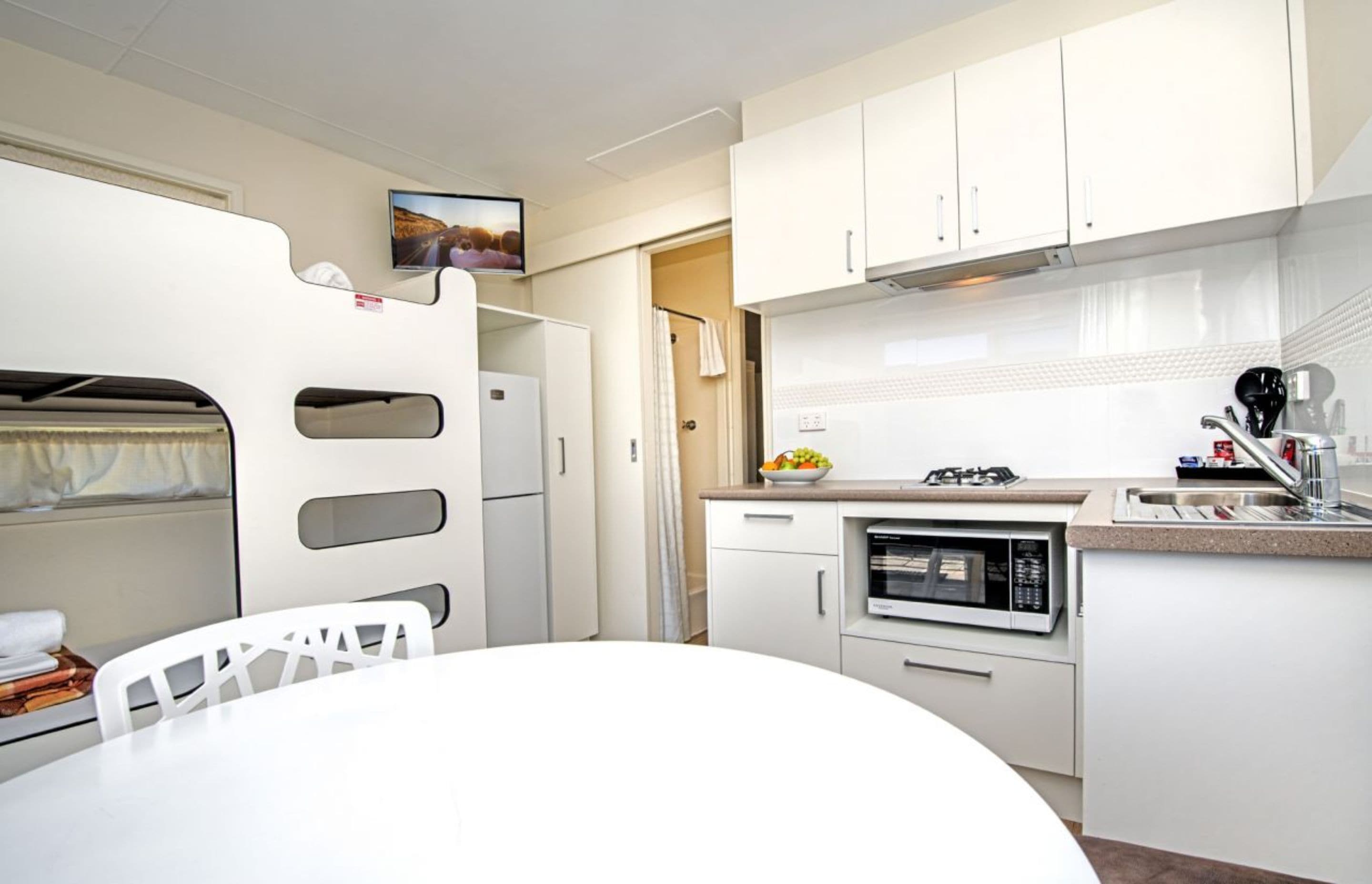 A compact kitchen with white cabinets, a microwave, a sink, and a small countertop.