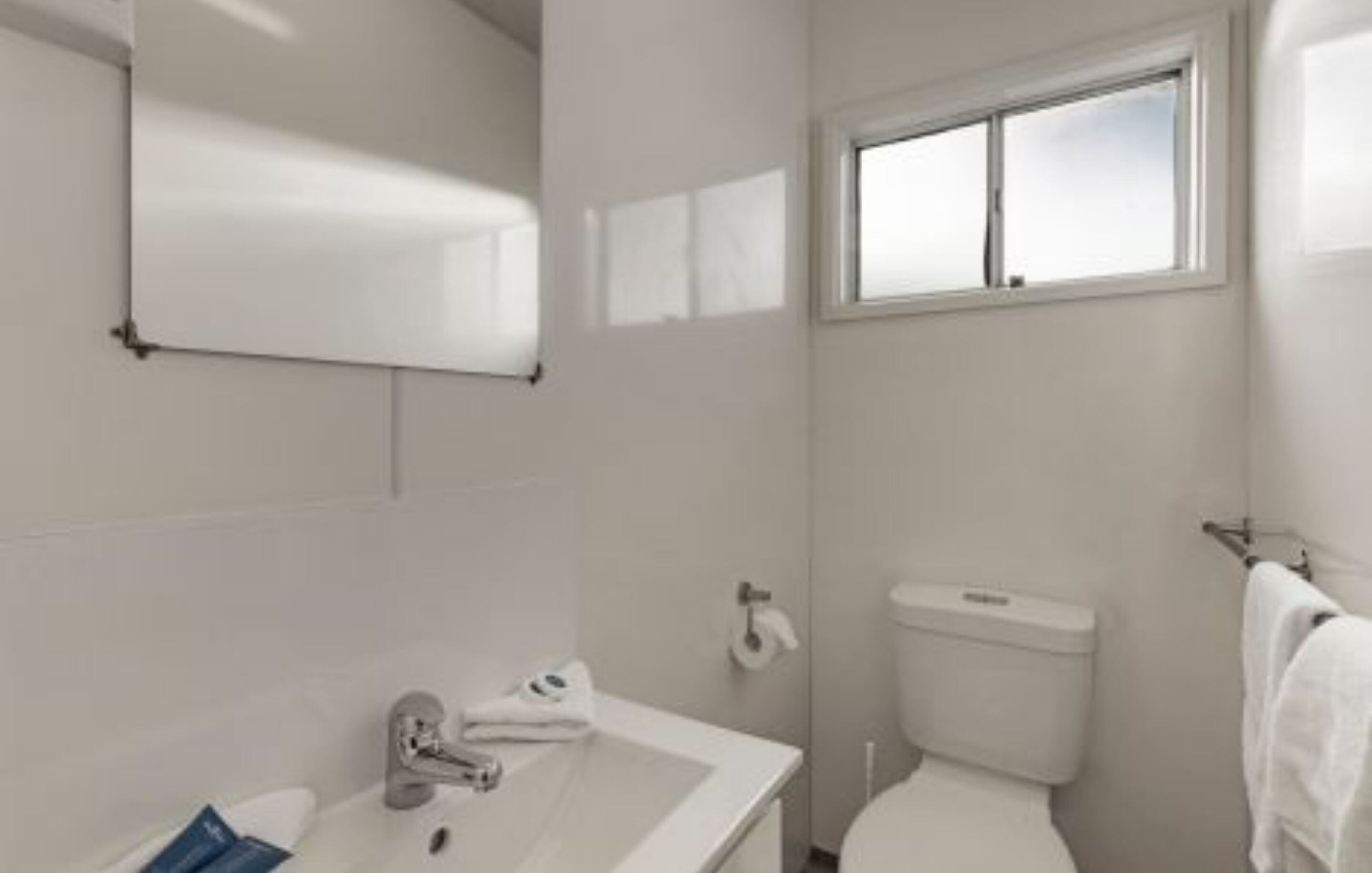 A small, clean bathroom with a white sink, toilet, and window.