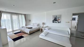 Un dormitorio moderno con dos camas, un ventanal con cortinas, un cuadro en la pared y una mesita de noche con una lámpara.