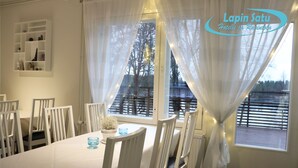 Ein Essbereich mit einem Tisch für vier Personen, weißen Stühlen, einem Blumentopf und einem Fenster mit Vorhängen.