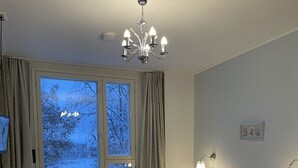 Ein Hotelzimmer mit zwei Betten, einem fensterbelaubten Fenster, einer Heizung, einem Sessel, einem Fernseher und einer Deckenleuchte.