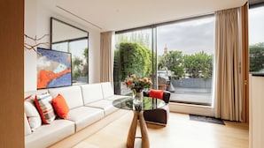 A modern living room with a white sofa, a glass coffee table, and a vase of flowers. - Le Cinq Codet (Paris)