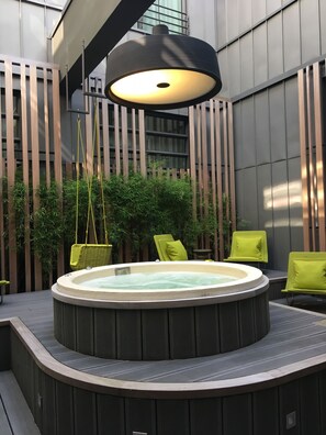 A hot tub surrounded by wooden slats and green plants, with a hanging light fixture above.