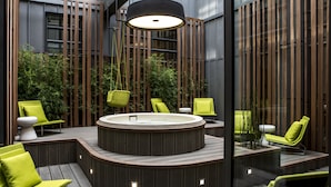 A modern outdoor hot tub area with wooden decking, green chairs, and a large overhead light. - Le Cinq Codet (Paris)