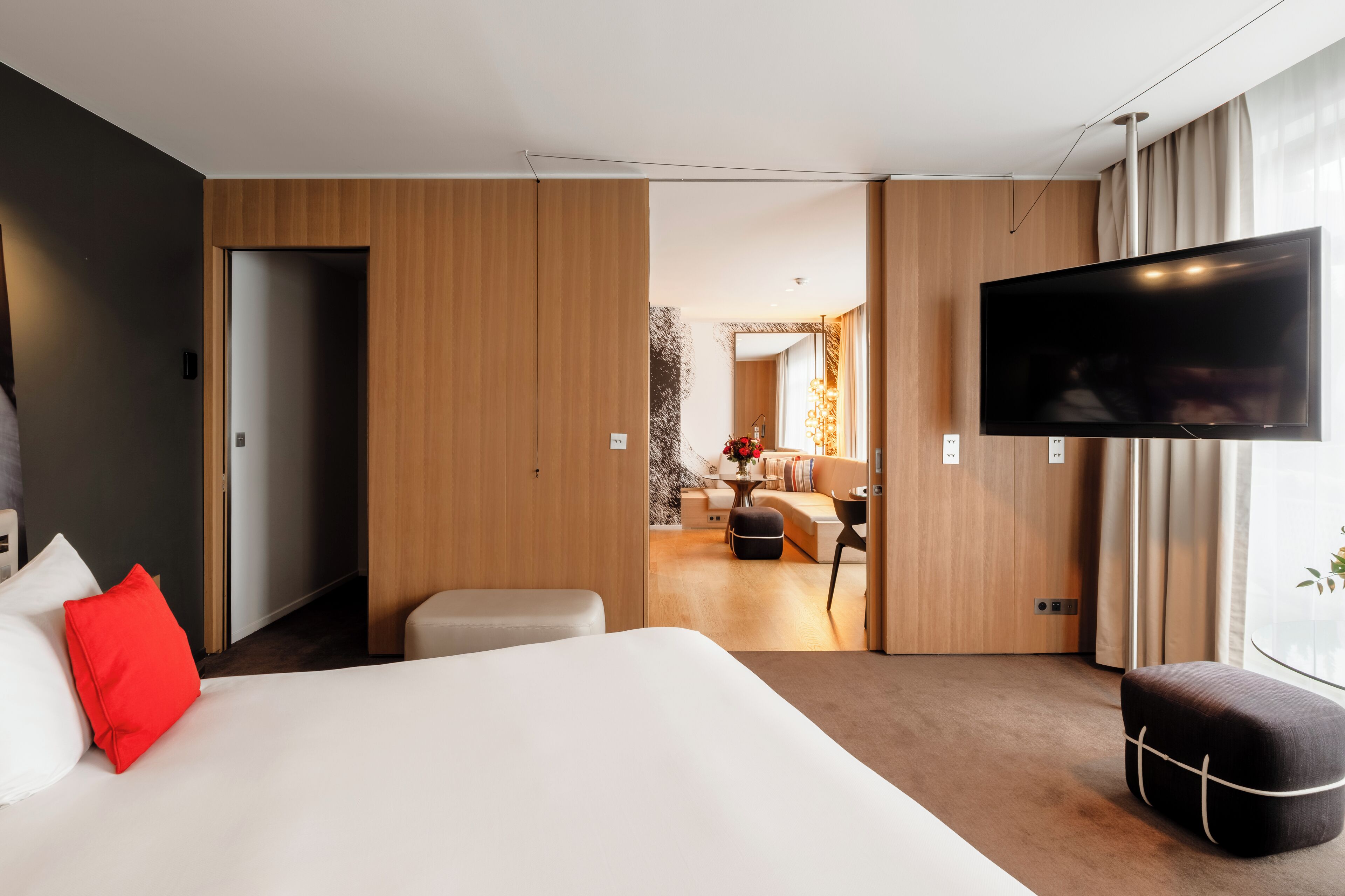 A modern hotel room with a large bed, a TV, and a view into the living area.