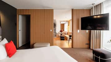 A modern hotel room with a large bed, a TV, and a view into the living area.