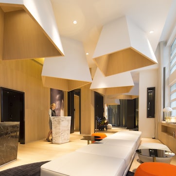A modern hotel lobby with a marble reception desk, a sofa, and a dining area.