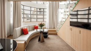 A modern living room with a curved sofa, a round coffee table, and a large window with a view of buildings. - Le Cinq Codet (Paris)