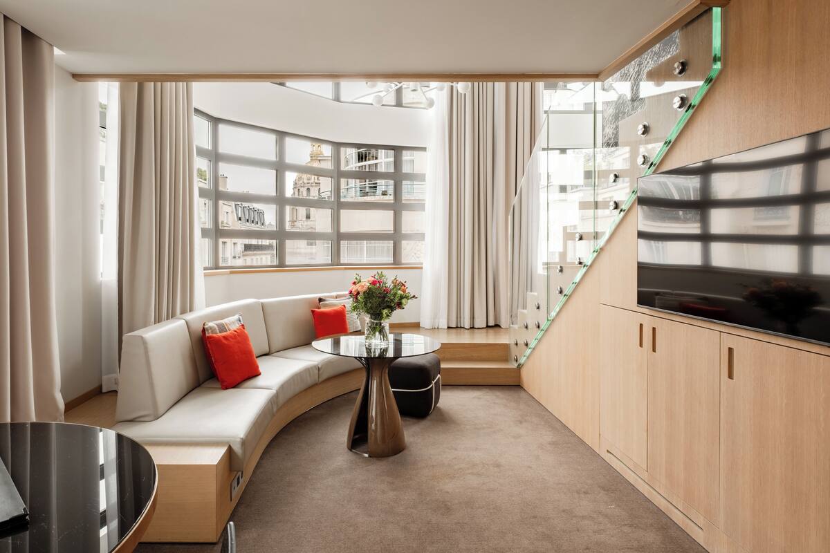 A modern living room with a curved sofa, a round coffee table, and a large window with a view of buildings.