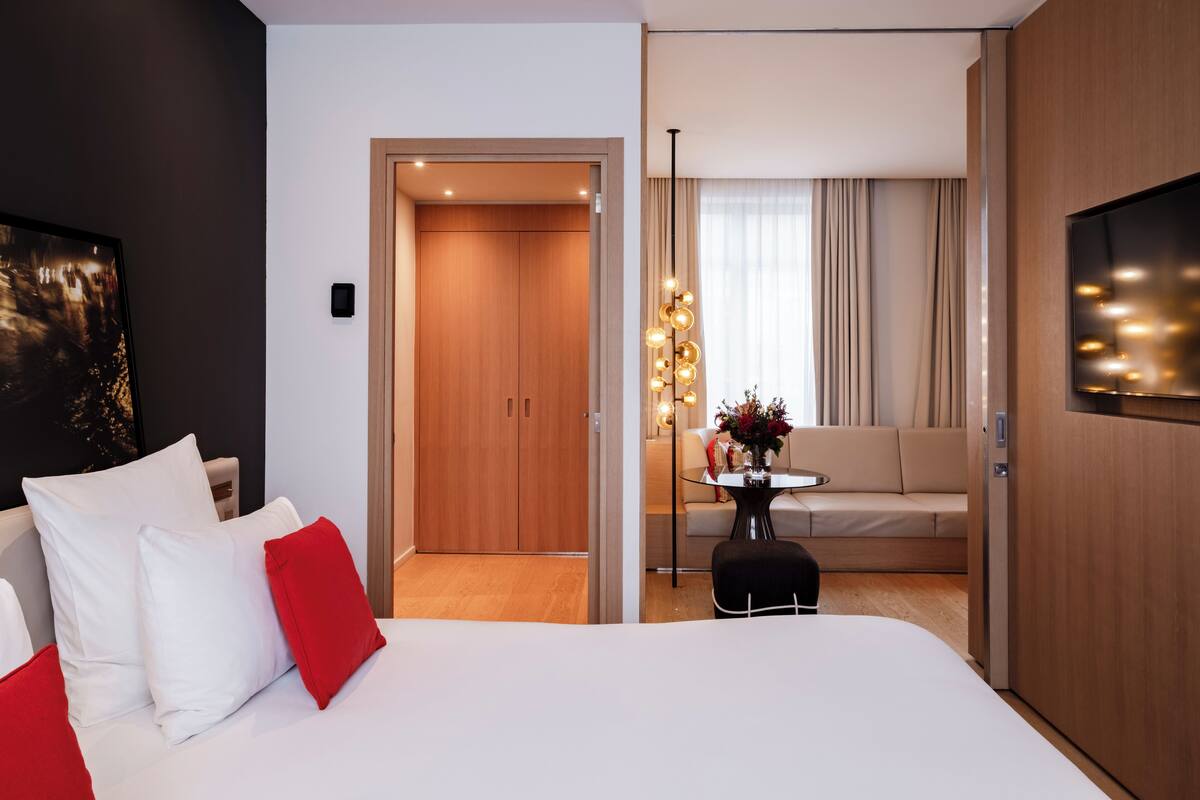 A hotel room with a large bed, a sofa, a TV, and a door leading to a hallway.