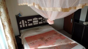 Un lit simple avec une tête de lit, une moustiquaire et une couvre-lit à motifs floraux.
