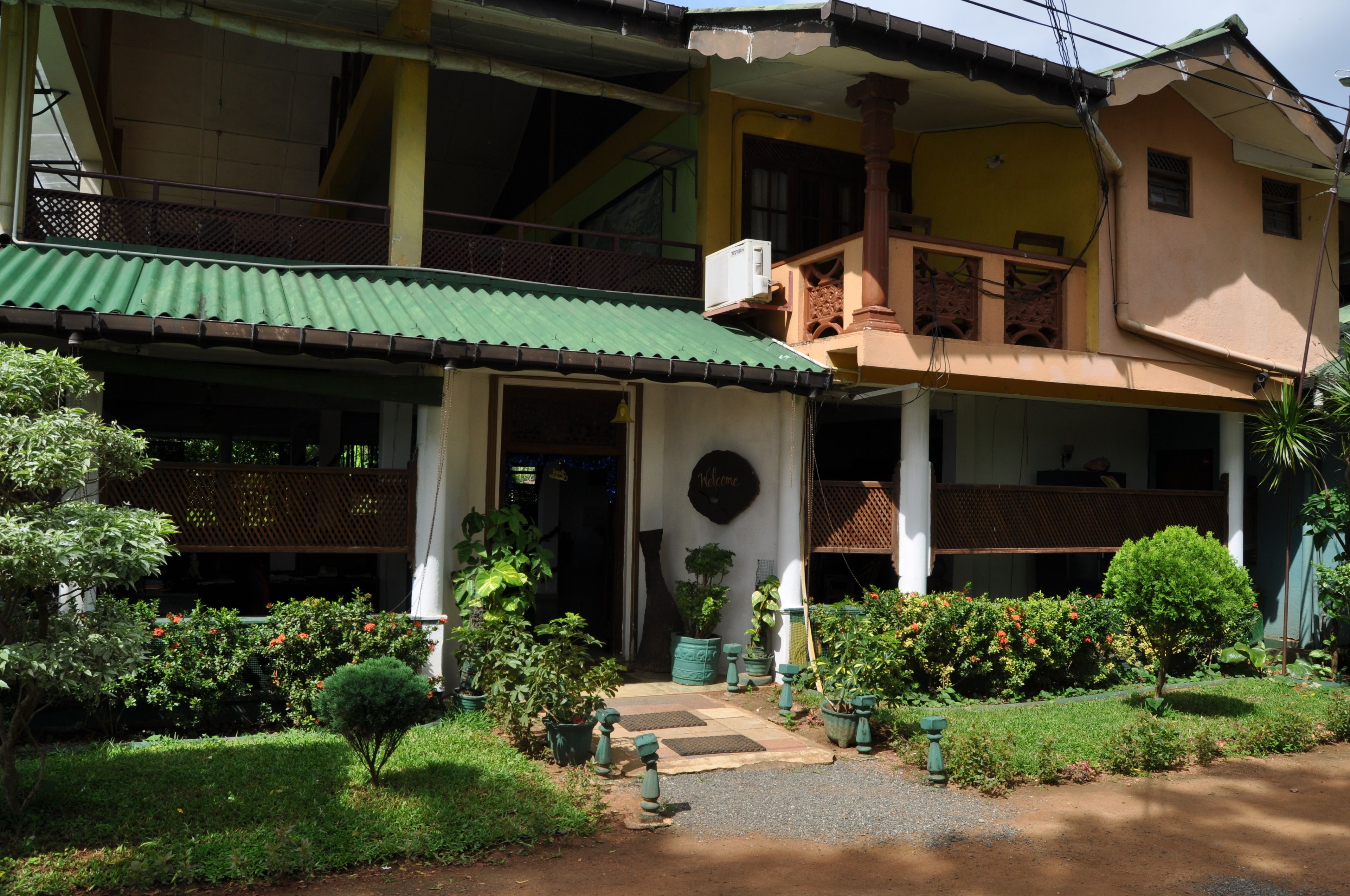 A two-story building with a green roof, a balcony, and a well-maintained garden with potted plants and a pathway.