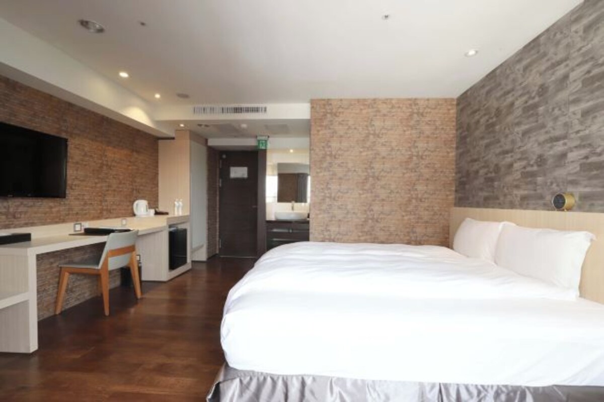 A modern hotel room with a large bed, a desk, and a flat-screen TV.