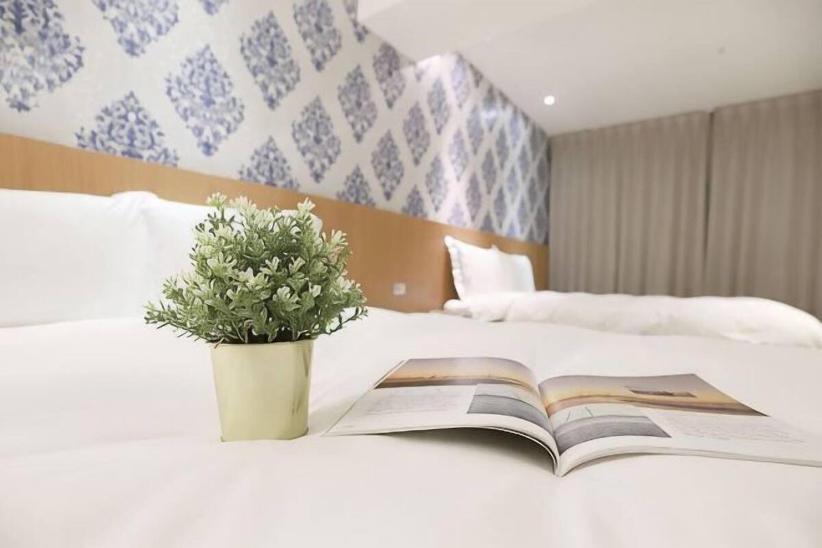 A hotel room with a bed, a potted plant, and an open magazine.