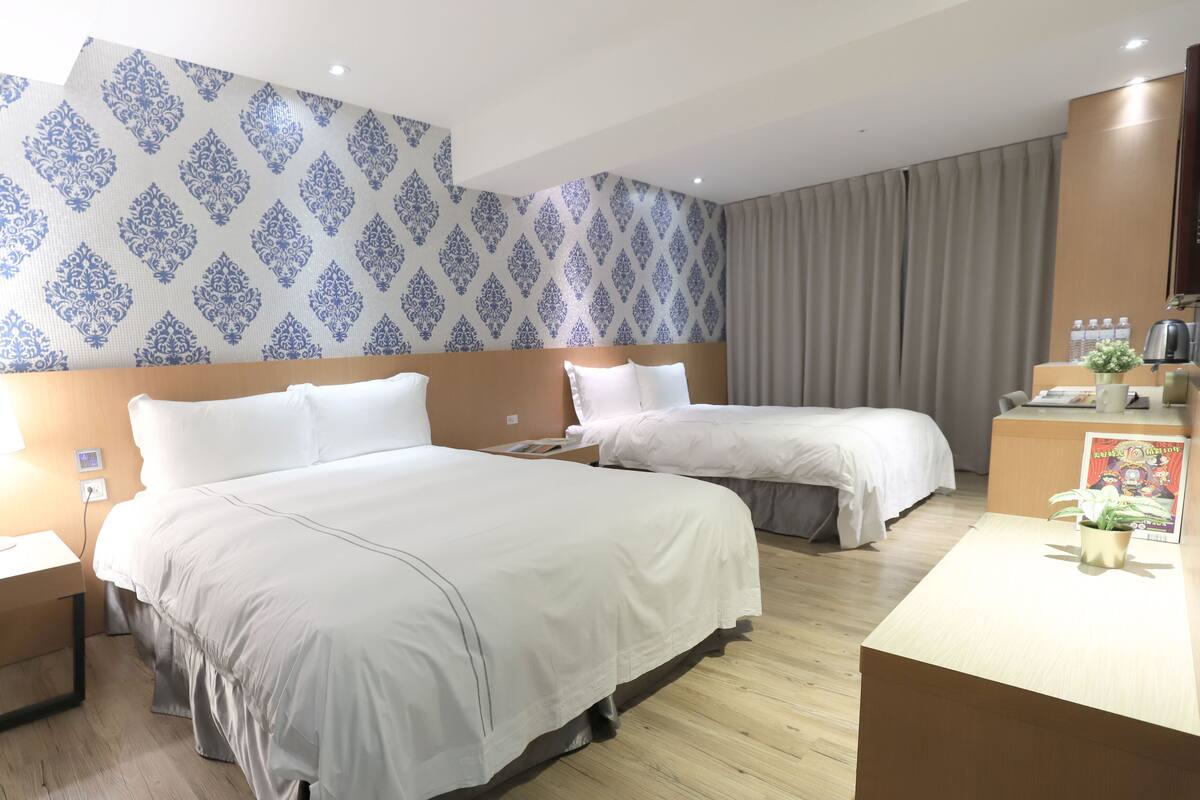 A hotel room with two beds, a desk, and a wall with patterned wallpaper.