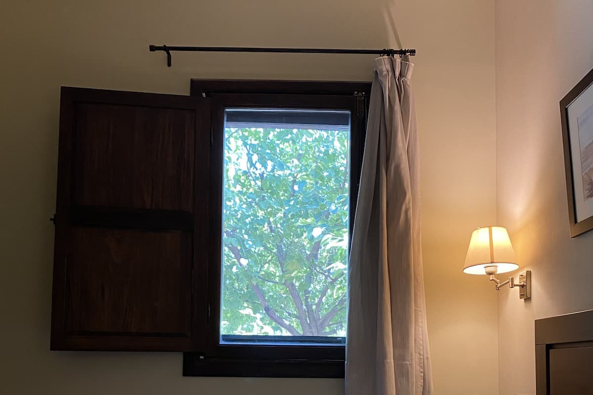 Un dormitorio con una cama, una ventana con cortinas, una lámpara de pared y un armario de madera.