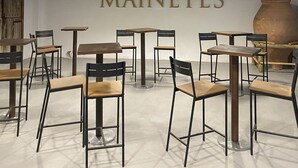 Interior de un restaurante con mesas y sillas, un cartel grande que dice "BODEGAS MAINETES" e iluminación colgante.