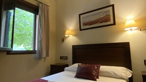 Un dormitorio con una cama, un ventanal, un cuadro y dos lámparas fijadas a la pared.