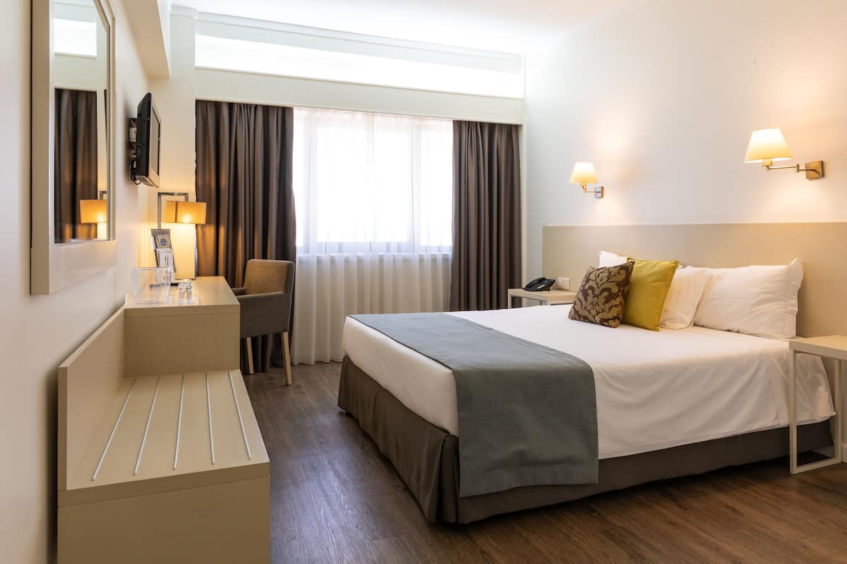 A hotel room with a bed, bedside table, chair, desk, and a large mirror.