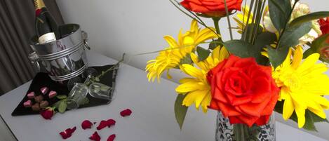 Una mesa con un florero de flores, una botella de champán y pétalos de rosa esparcidos.