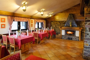 A dining area with red tables and chairs, a stone fireplace, and a wooden ceiling. - Hotel Planja - Rogla (Zrece)